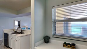 A modern kitchen with white cabinets, a sink, and a window with blinds. - Pelican Isle #513 | Seasonal Beach Service + Resort Amenities (Fort Walton Beach)
