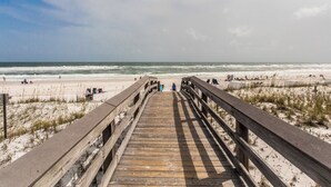 A wooden boardwalk leading to a beach with people and beach chairs. - Pelican Isle #513 | Seasonal Beach Service + Resort Amenities (Fort Walton Beach)