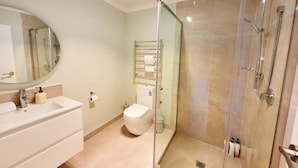 Een moderne badkamer met een douchecabine van glas, een wit wastafeltje en een toilet.