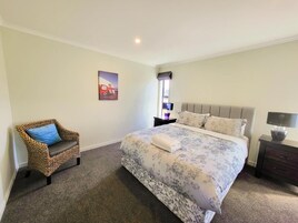 Un dormitorio con una cama grande, una silla, una mesita de noche y una lámpara de pared.
