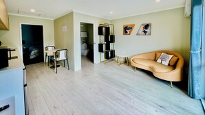 Een moderne woonkamer met een bank, een kleine tafel en een tv-meubel. Er is een deur naar een badkamer en een trap.