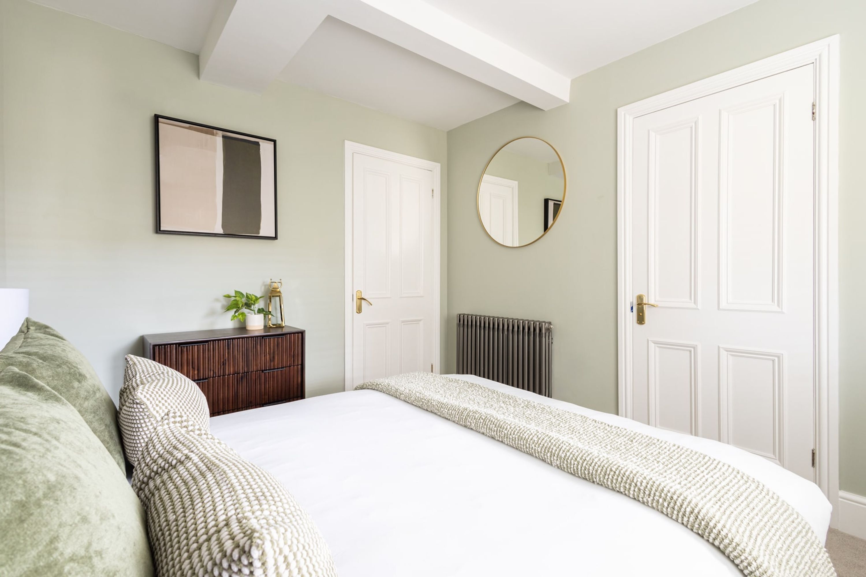 A bedroom with a large bed, a dresser, a mirror, and two doors.