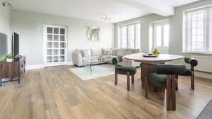 Ein geräumiges Wohnzimmer mit Holzboden, einem weißen Sofa, einem runden Esstisch und einem grünen Akzentstuhl.