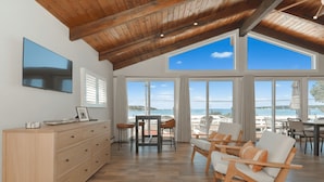 Un vaste espace de vie doté d’un plafond en bois, de grandes fenêtres offrant une vue sur la mer, d’un meuble en bois et de sièges confortables.