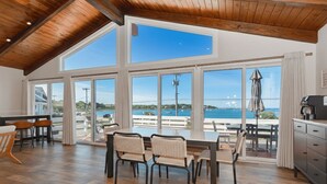 Un vaste espace dédié à la salle à manger, avec une grande table et des chaises, de grandes fenêtres offrant une vue sur la mer et un plafond en bois.
