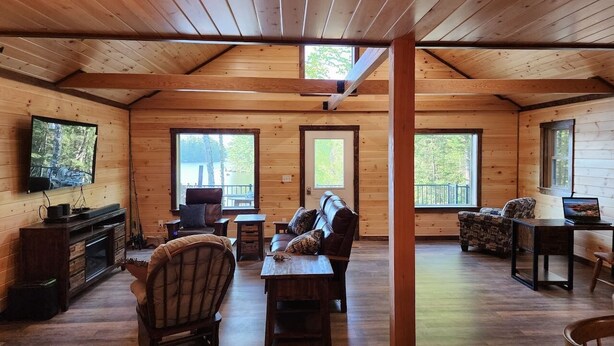 A cabin interior with wooden walls, a TV, a fireplace, and a large window.