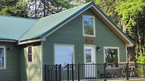 A green building with a metal roof, a wooden deck, and a black railing.