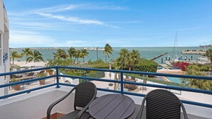 A balcony with two wicker chairs and a table, overlooking a marina with boats and palm trees. - An Ocean Serenity at the Truman Annex in Key West (Key West)