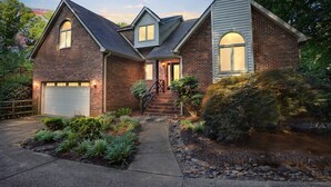 Une maison à deux étages, construite en briques, avec un garage à l’avant, un porche couvert et un jardin aménagé avec un chemin menant à l’entrée.