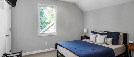 A bedroom with a bed, a window with blinds, a ceiling fan, and a TV mounted on the wall.