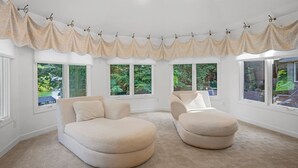 Une pièce avec deux canapés de couleur beige, un lambrequin décoratif et de grandes fenêtres donnant sur un paysage verdoyant.