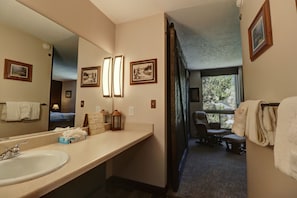 Une salle de bain d’hôtel équipée d’un grand miroir, d’un lavabo, d’un porte-serviettes et d’un fauteuil de massage.