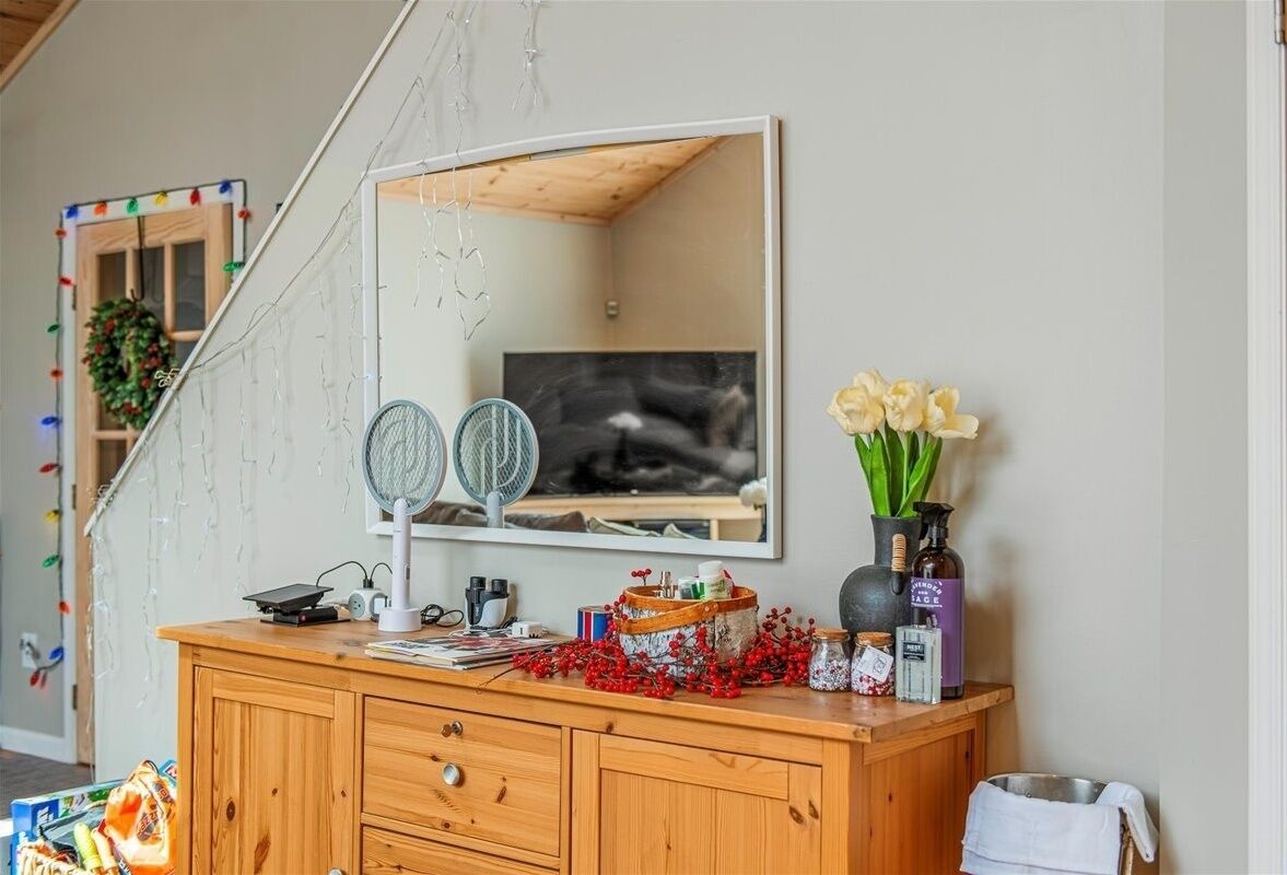 A wooden vanity with a mirror, a fan, and decorative items including a vase with flowers and a basket of red berries.