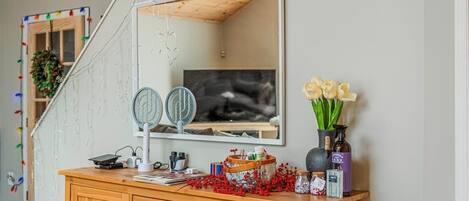 A wooden vanity with a mirror, a fan, and decorative items including a vase with flowers and a basket of red berries.