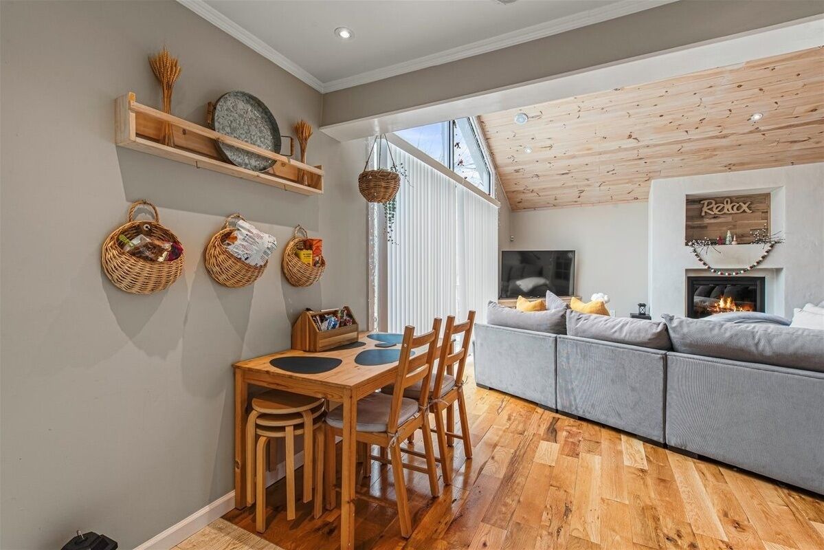 Een gezellige woonkamer met een open haard, houten plafond en een grijze bank.