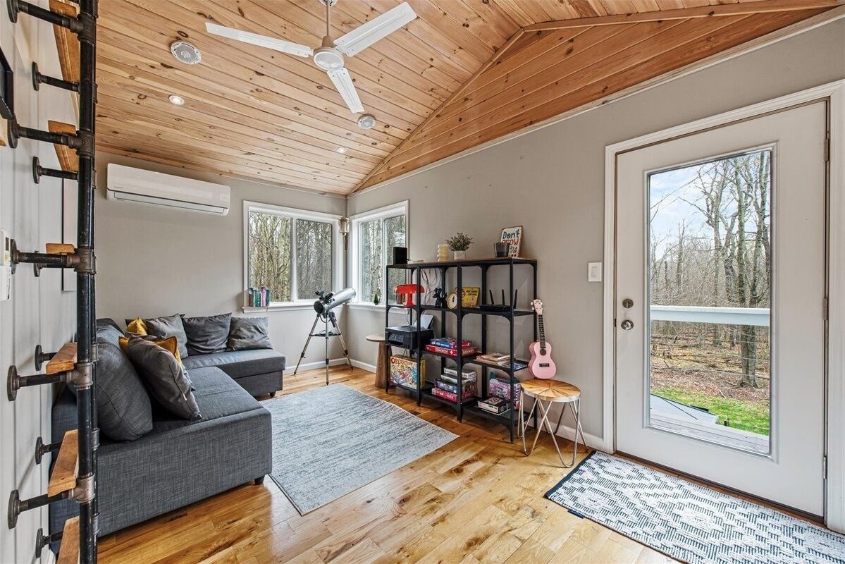 Ein modernes Wohnzimmer mit Holzboden, einem grauen Sofa, einem Bücherregal und einer Gitarre.