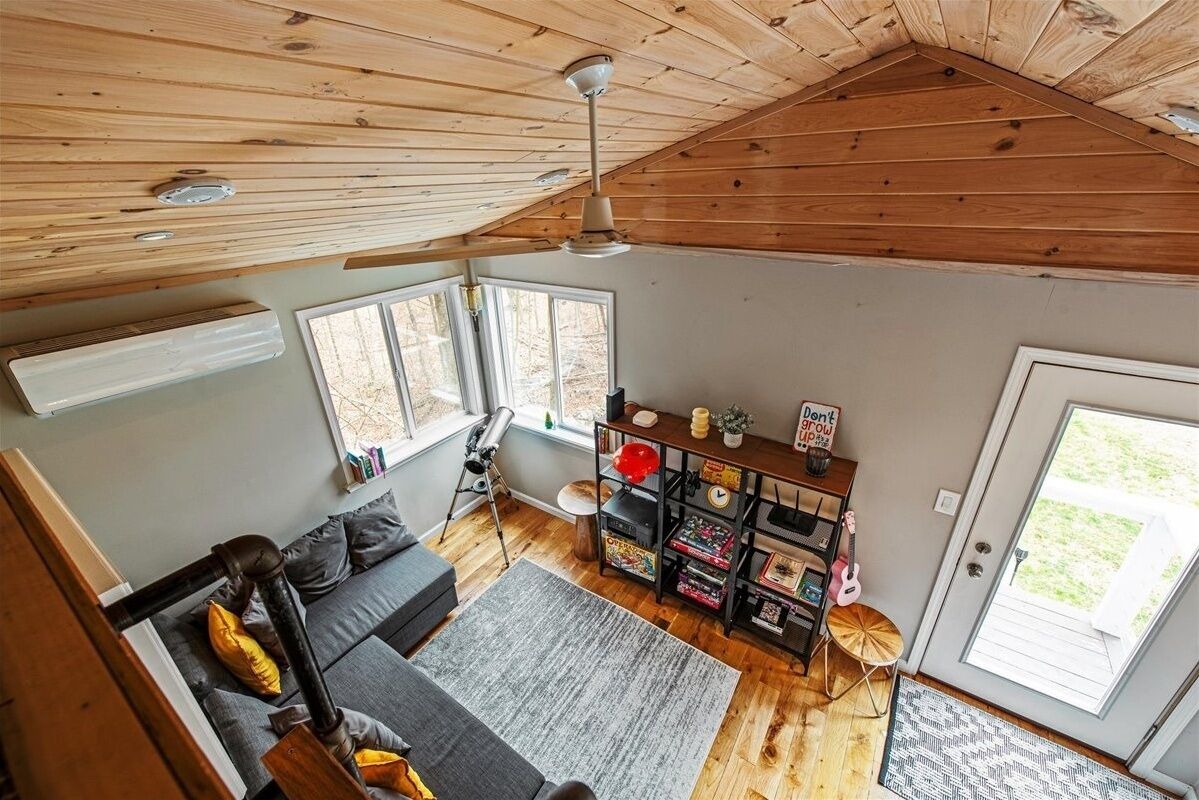 A loft-style room with a sloped ceiling, a sofa, a desk with books and a guitar, and a large window.