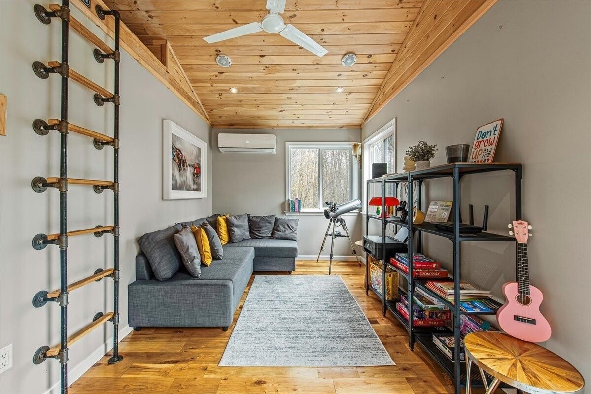 A cozy living room with a grey sofa, a telescope, a bookshelf, and a guitar.