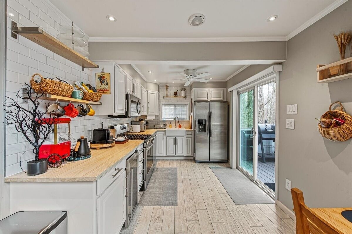 A modern kitchen with white cabinets, a wooden countertop, and a stainless steel refrigerator.