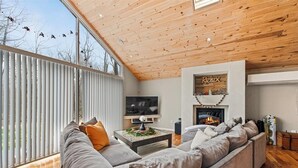 Een moderne woonkamer met een groot houten plafond, een grijze bank, een flatscreen televisie en een open haard.