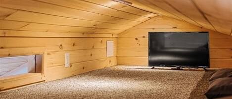 A small attic room with a television, a window, and a carpeted floor.