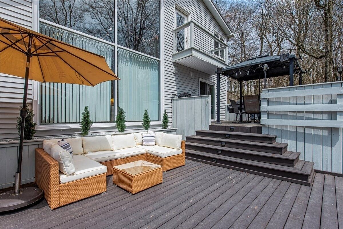 Una terraza con sofá y sombrilla, un área cubierta con mesa, y una escalera que conduce a otra terraza.