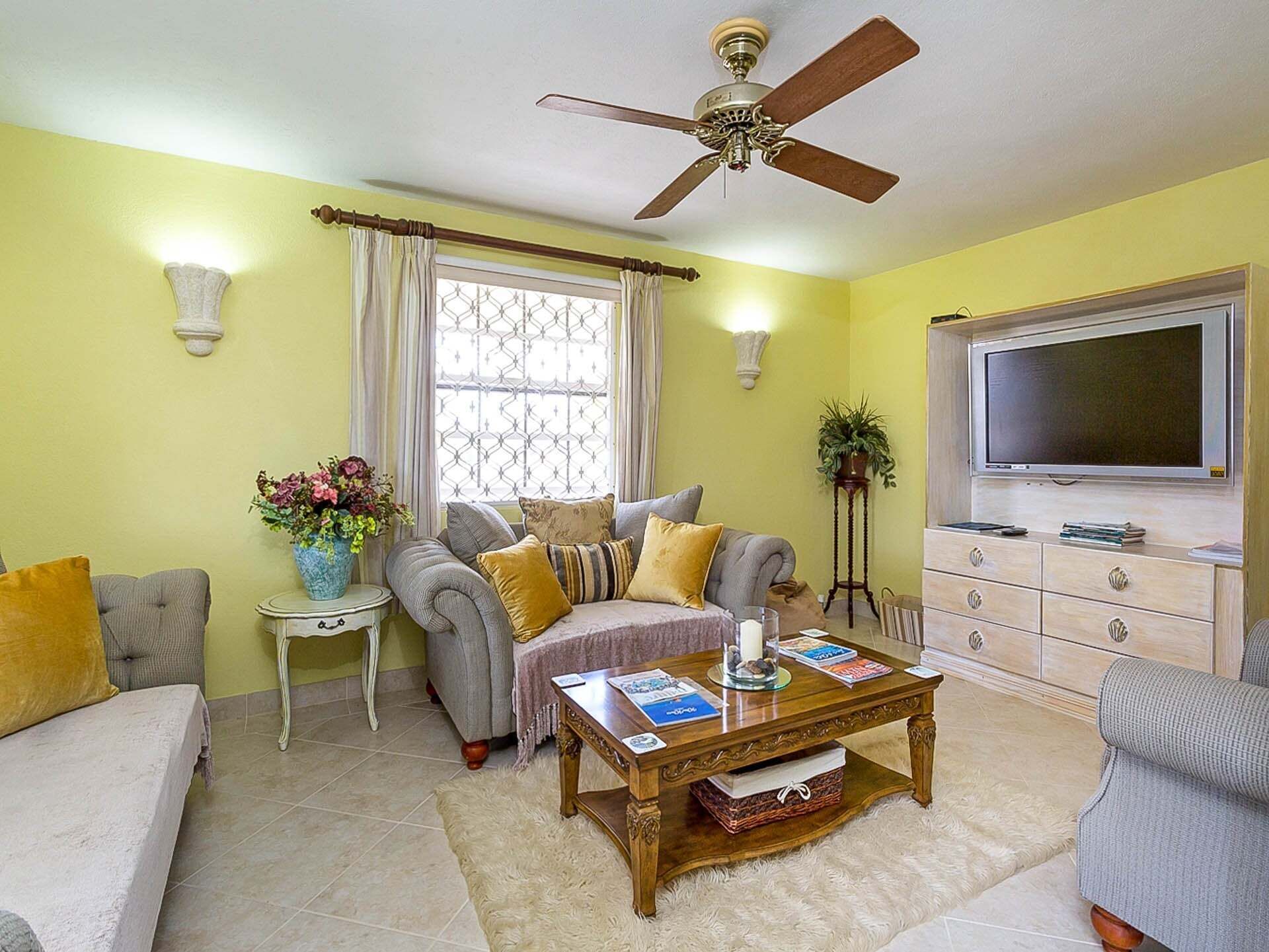 A living room with a sofa, a coffee table, a television, a ceiling fan, and a window with curtains.