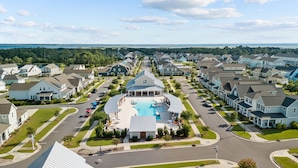 Un quartier résidentiel avec des maisons, une piscine centrale et une vue sur l’océan.