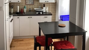 Cocina compacta con armarios blancos, encimera negra y una pequeña mesa de comedor con cojines rojos.