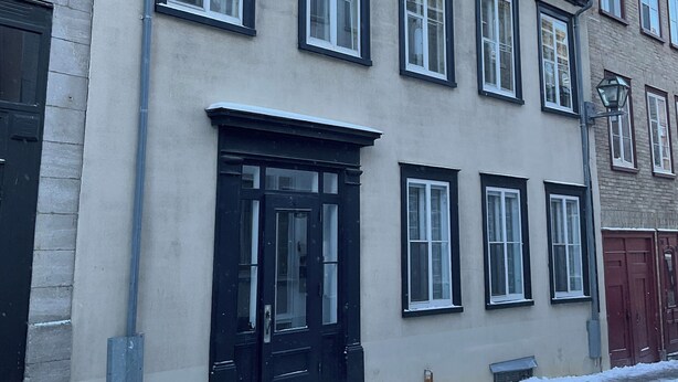 Un edificio de varios pisos con puerta principal negra, múltiples ventanas y fachada de ladrillo.