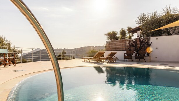 Una piscina cristalina con sillones de descanso y vistas a colinas.