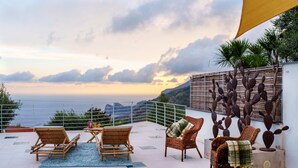 Una terraza con mobiliario de mimbre, una escultura de cactus y vista al mar.