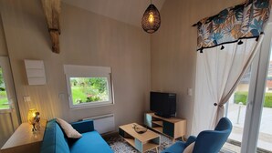 A modern living room with a blue sofa, a television, and a window with a garden view. - The Blue Tit (Ognes)