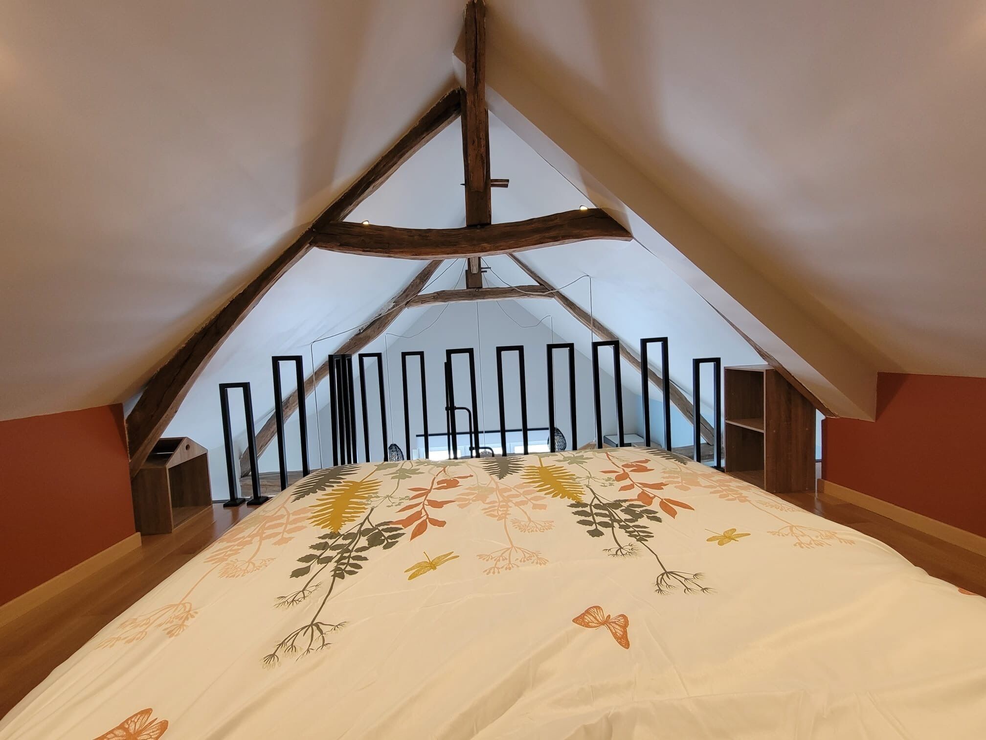 A bedroom with a sloped ceiling, a bed with a floral bedspread, and a view of the outside through a window.