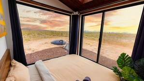 A bedroom with a large window offering a view of a desert landscape. - Grand Canyon Stargazing Off-Grid Tiny Home (Williams)