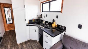 A compact kitchen with white cabinets, a black countertop, and a window above the sink. - Grand Canyon Stargazing Off-Grid Tiny Home (Williams)