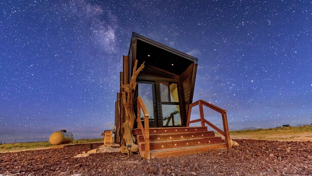 A rustic cabin with a wooden exterior, a glass door, and a wooden staircase leading up to a porch. - Grand Canyon Stargazing Off-Grid Tiny Home (Williams)
