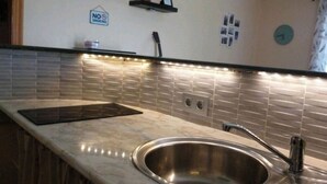 Una cocina moderna con un lavamanos de acero inoxidable, encimera negra y salpicadero de azulejos.