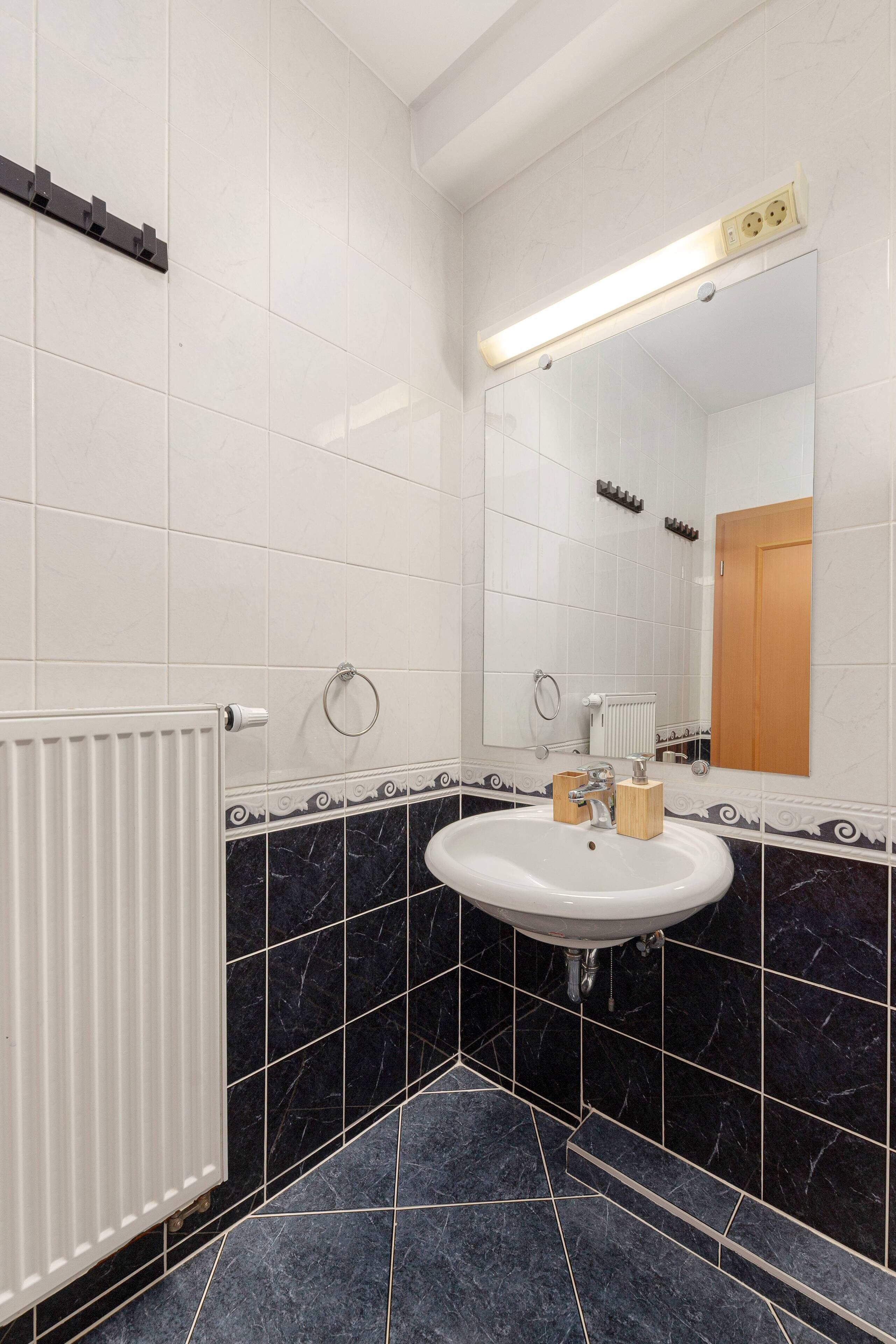 Une salle de bain avec un lavabo blanc, des carreaux de marbre noir, un miroir et un radiateur.