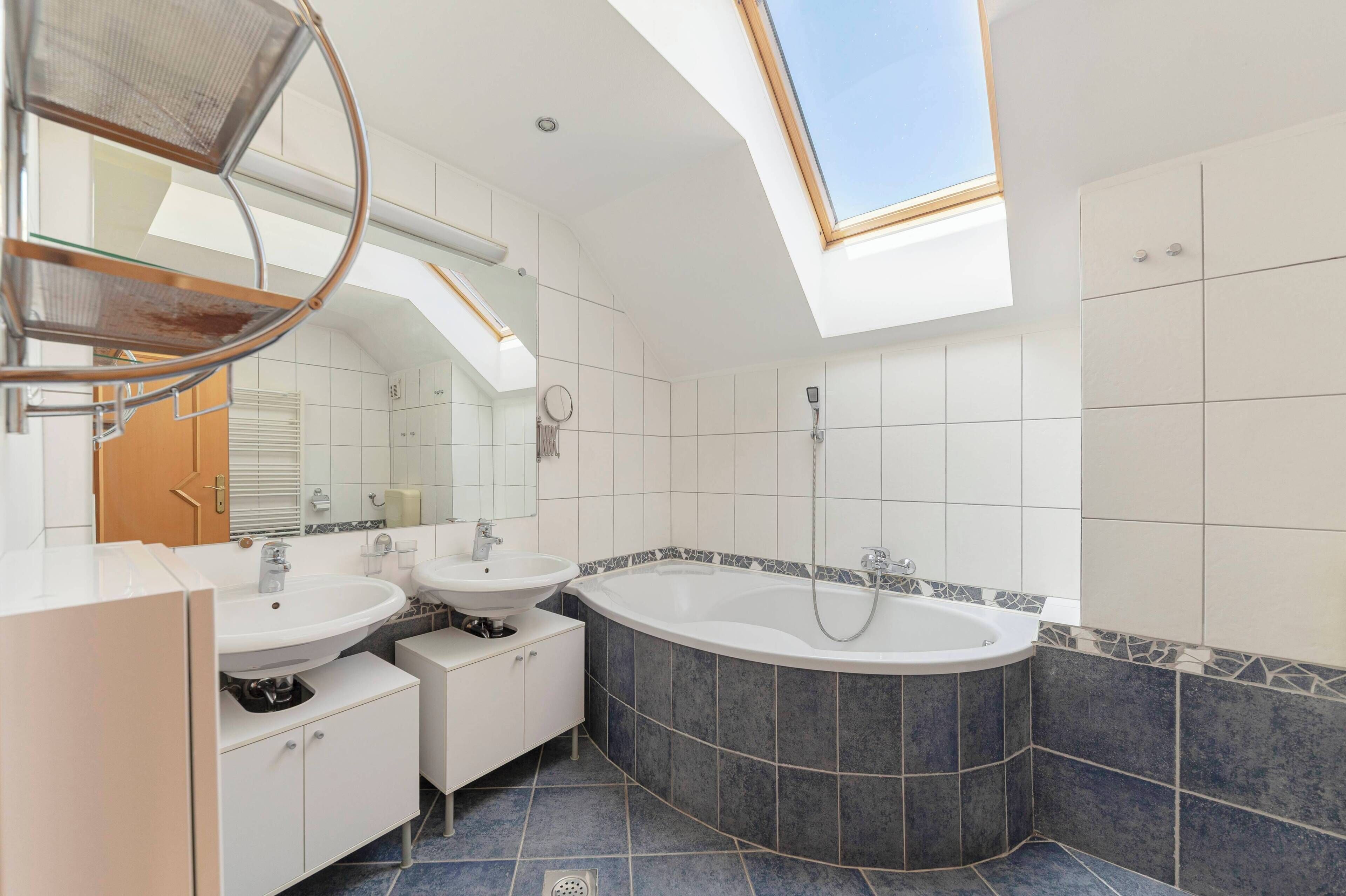 Une salle de bain moderne dotée d’une lucarne, de deux lavabos, d’une baignoire et d’une douche.