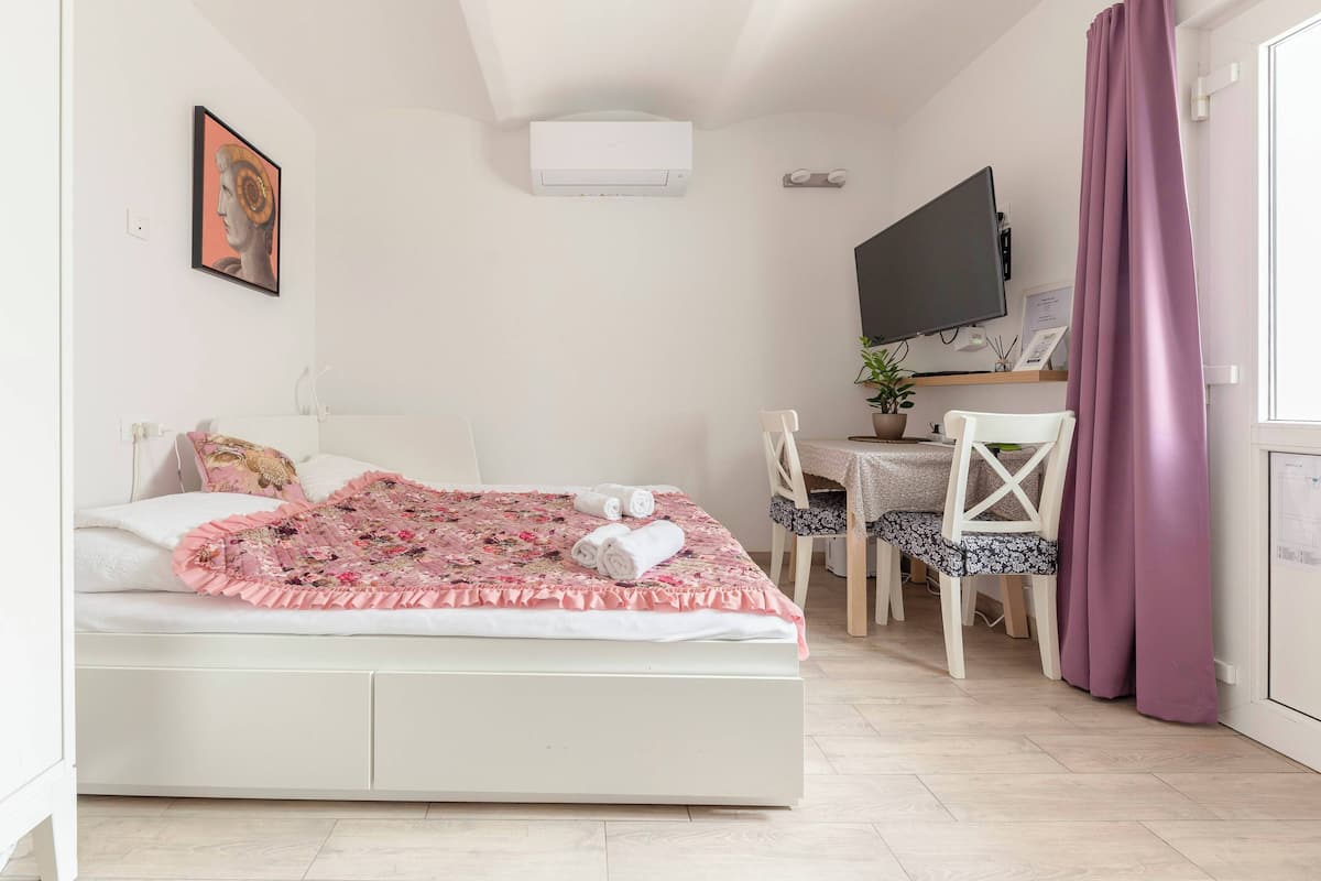 Un dormitorio con cama, escritorio, silla, televisor y ventana con cortinas.
