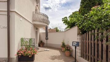 Un patio con zona ajardinada, plantas en macetas, cerca de madera y un cartel que indica zona de estacionamiento para huéspedes.