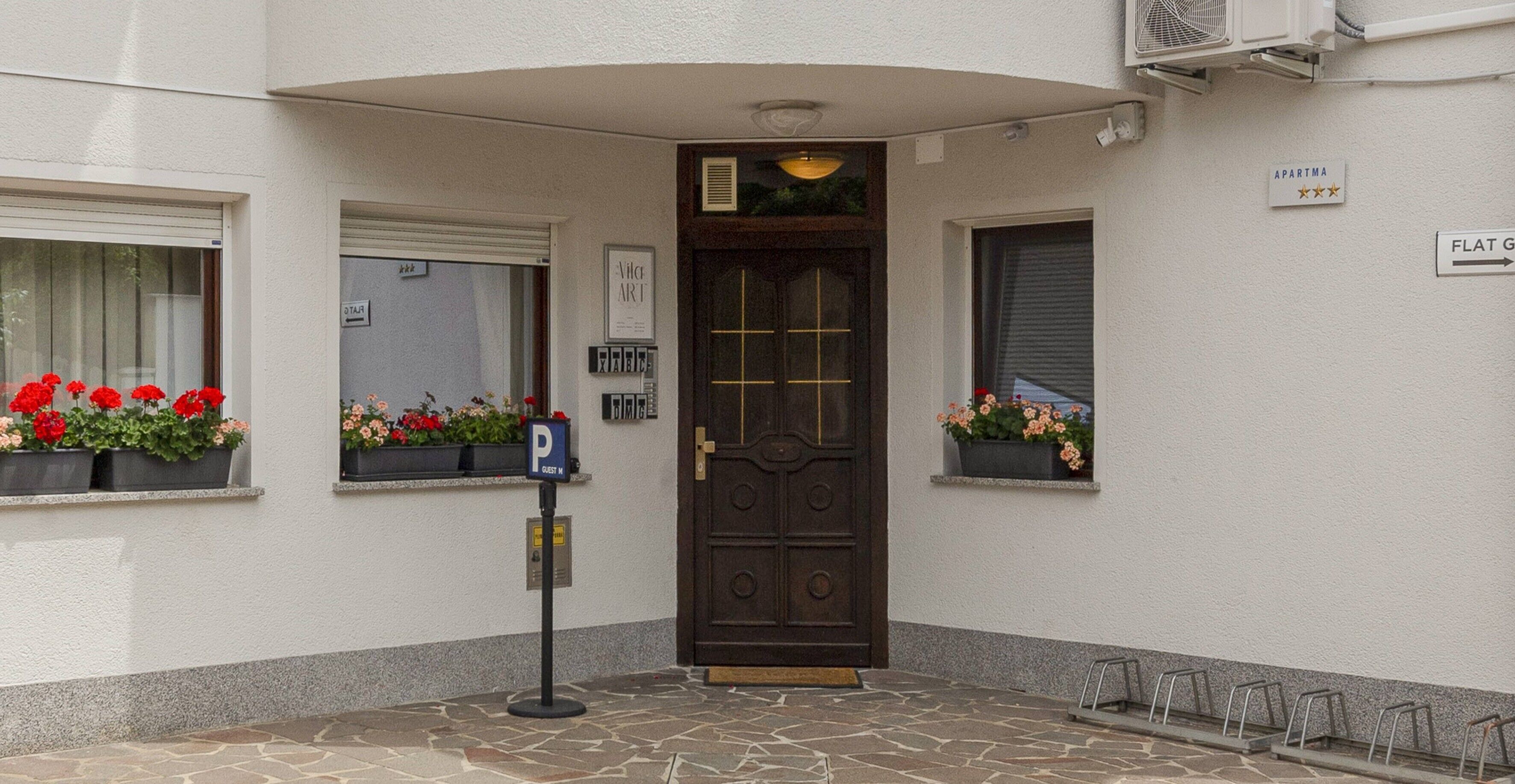 A building entrance with a dark wooden door, a parking sign, and flower boxes on the windowsills.