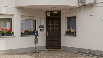 A building entrance with a dark wooden door, a parking sign, and flower boxes on the windowsills.
