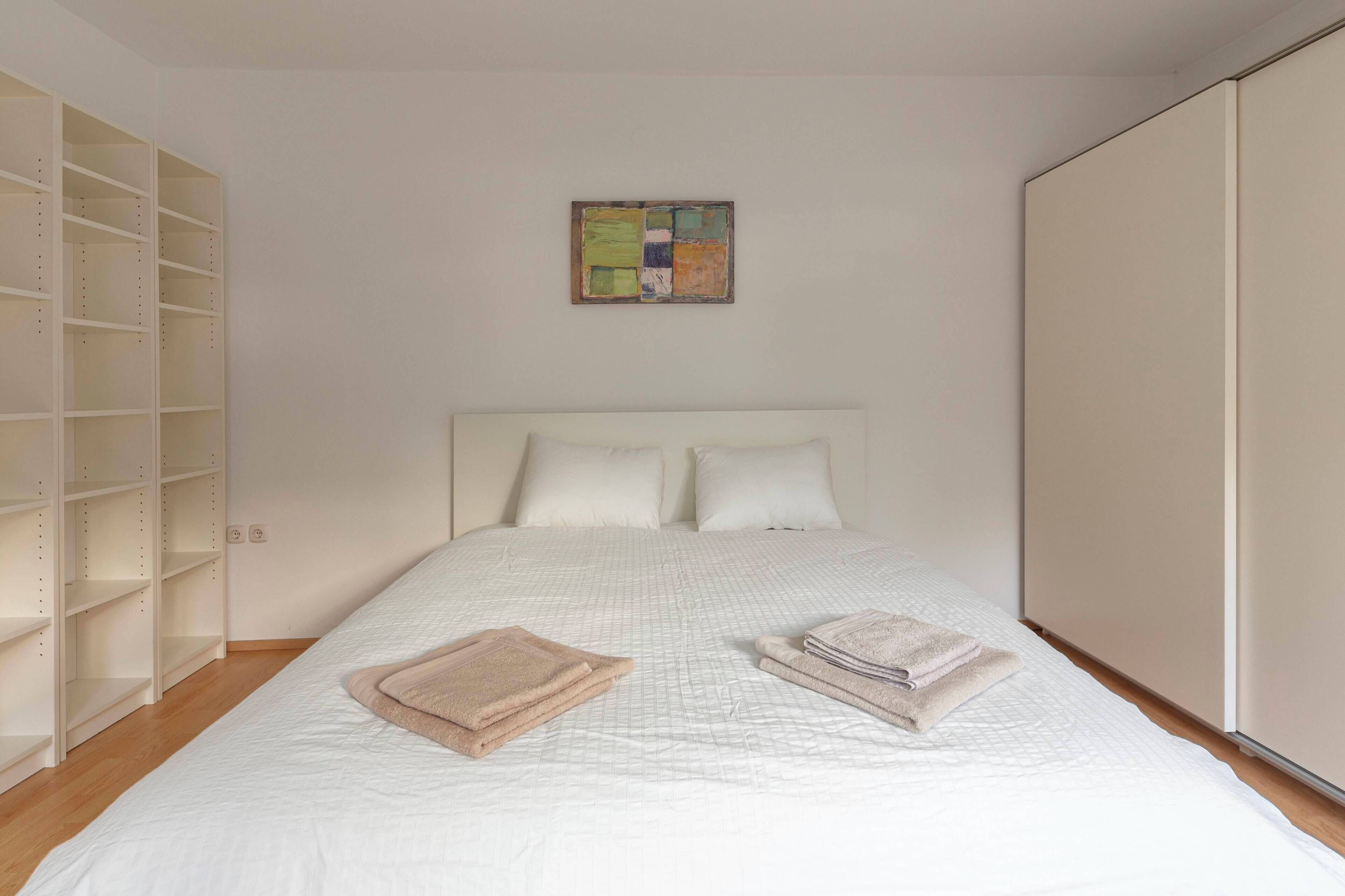 Une chambre bien rangée, avec un grand lit, une armoire et une petite œuvre d’art accrochée au mur.