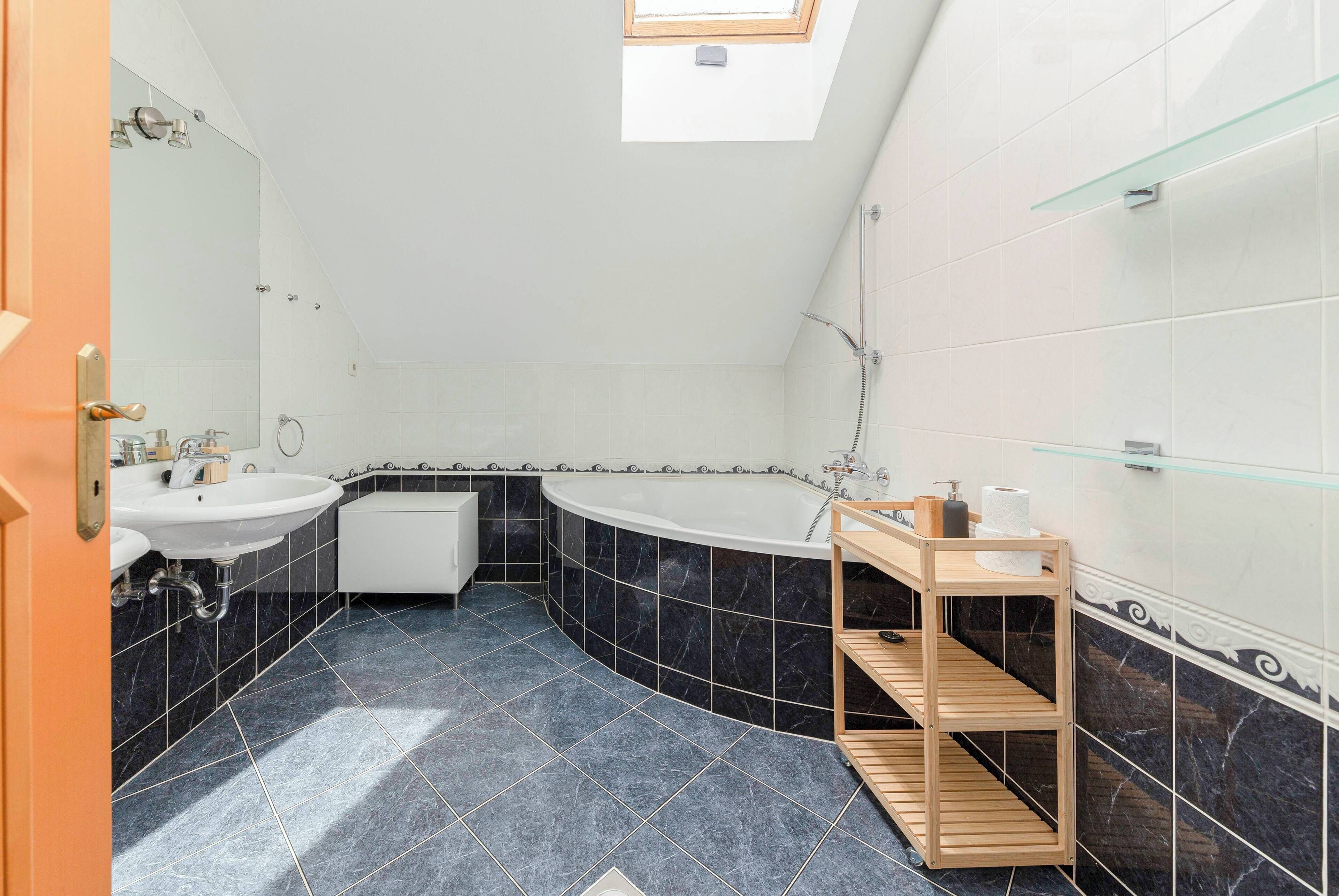 A bathroom with a freestanding bathtub, two sinks, a shower, and a skylight.