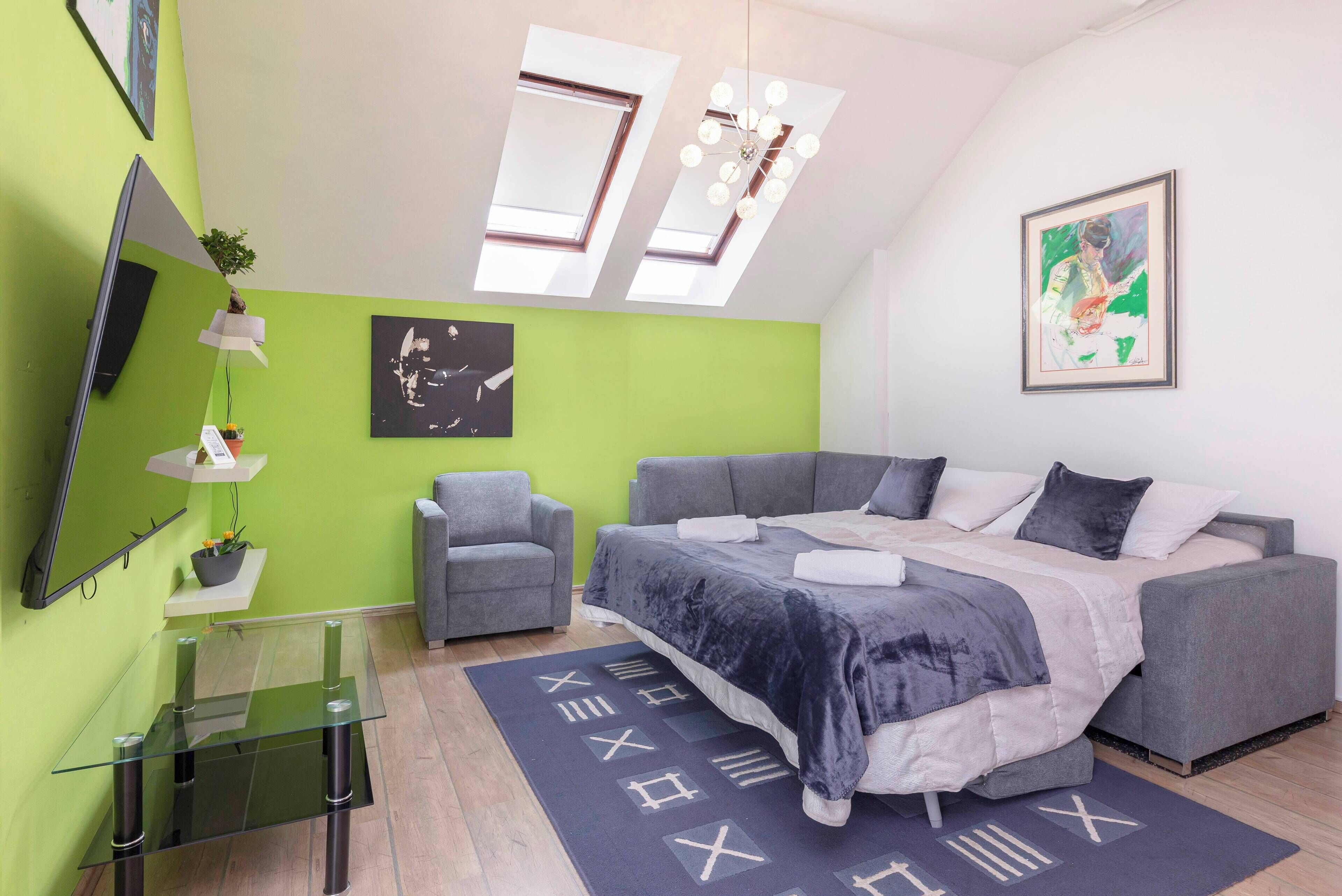Ein modernes Schlafzimmer mit einem großen Bett, einem grauen Sofa, einem Glastisch und einer grünen Akzentwand.