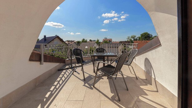 A balcony with a table and chairs, a view of houses, and a clear sky.