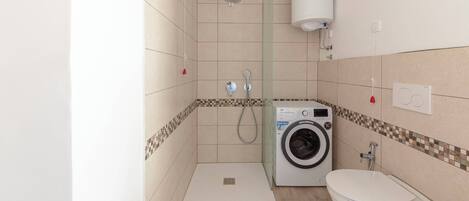 A compact bathroom with a shower, toilet, and washing machine.