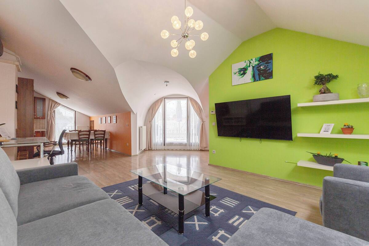 Una sala de estar moderna con una mesa de centro de vidrio, sofás grises y una pared de acento verde.